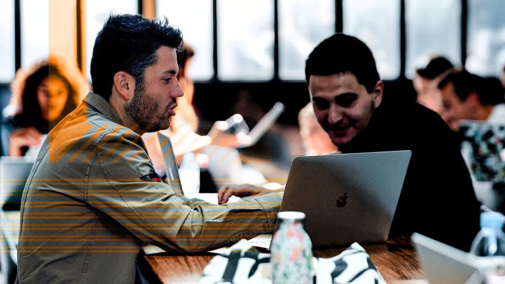 Two students talk in front of a MAC computer